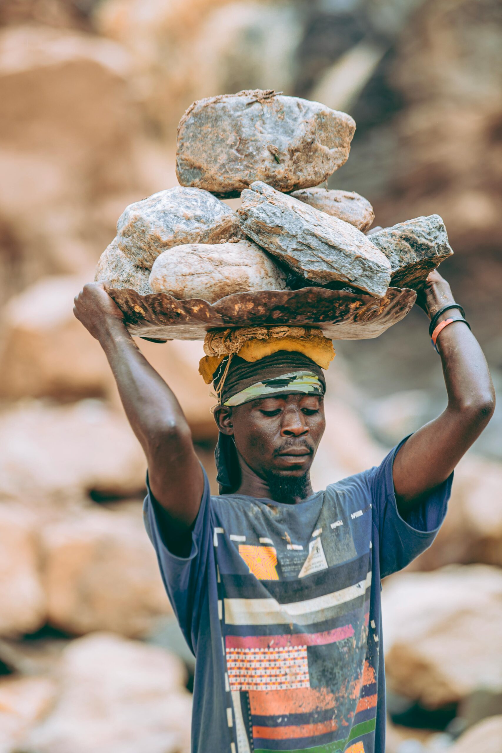 A man balances a basket of stones on his head in a quarry setting.